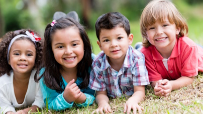 Vier lachende Kinder liegen auf dem Rasen