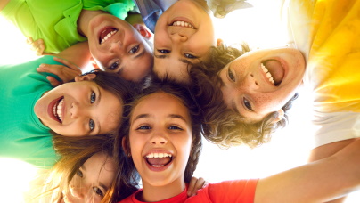 Symboldbild: Sechs Jugendliche mit bunten Tshirts stehen im Kreis und lachen nach unten in die Kamera (Ameinsenperspektive)