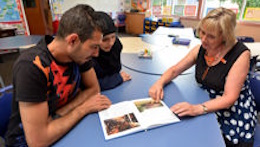 Bild Elternmentoren Eine Elternmentorin sitzt mit einer Frau und einem Mann an einem Tisch. Sie schauen in ein Buch.